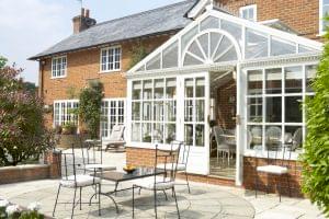 An elegant conservatory attached to a brick house, with outdoor seating on a patio