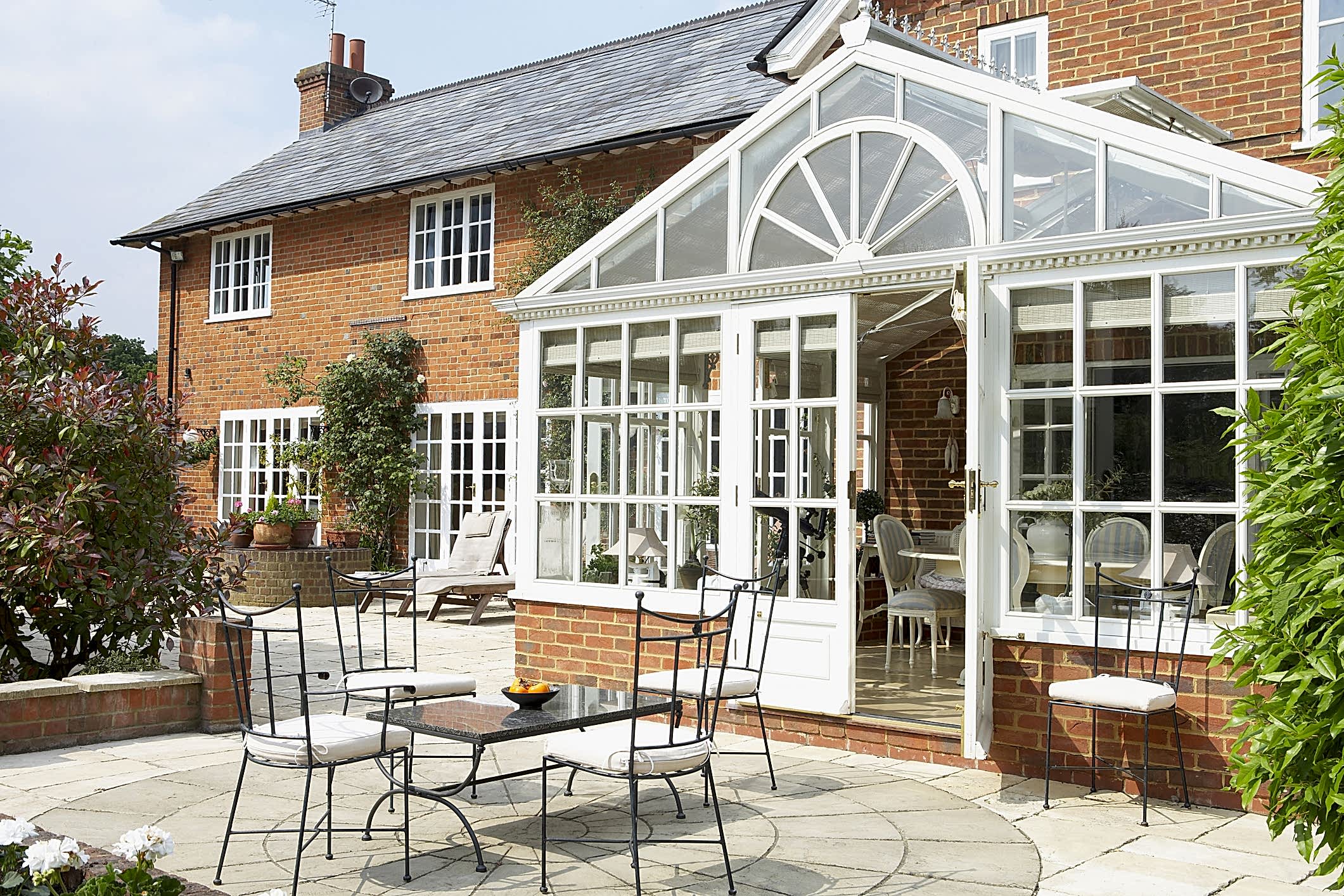 An elegant conservatory attached to a brick house, with outdoor seating on a patio